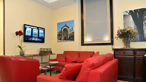 A living room with red sofas, a flat-screen TV, a vase with flowers, and a framed picture of a building. - Nuovo Albergo Italia (Abbiategrasso)