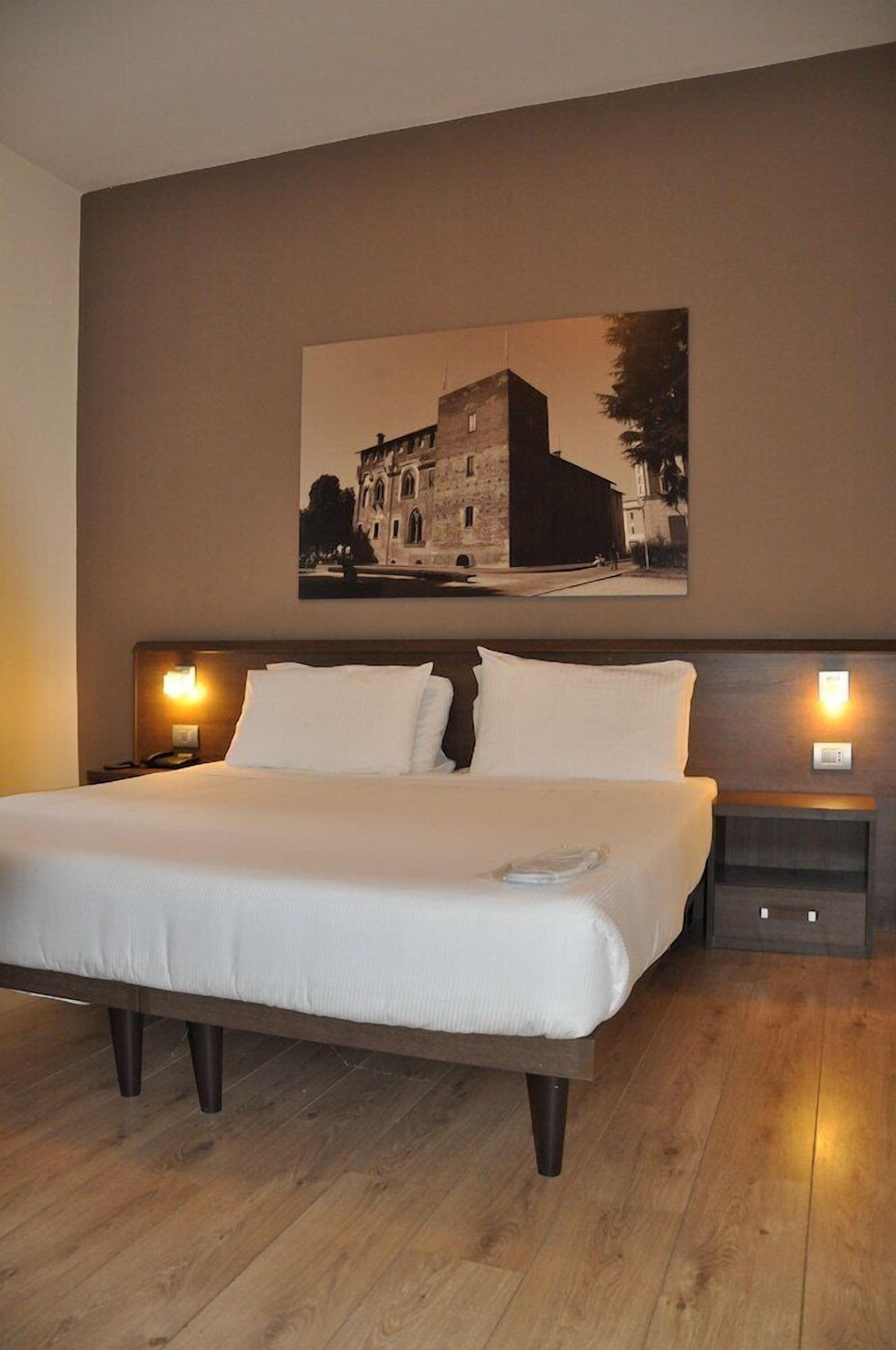 Una cama bien tendida en una habitación de hotel con un cuadro grande enmarcado sobre ella.