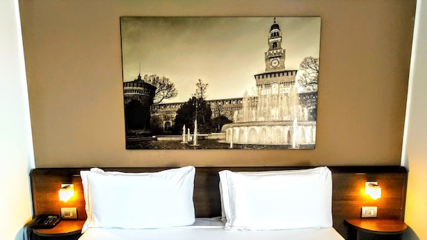 A hotel room with a large bed, two bedside tables with lamps, and a framed picture of a historic building on the wall. - Nuovo Hotel Italia (Abbiategrasso)
