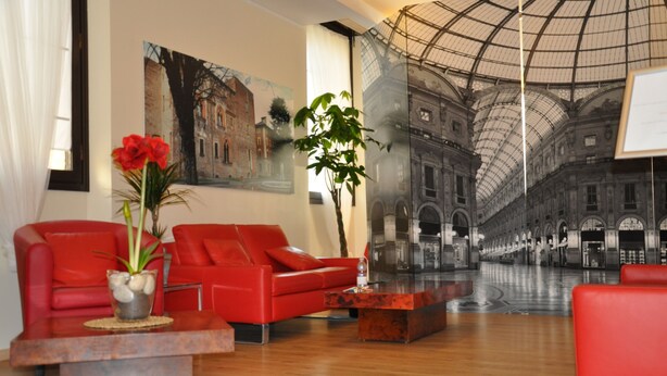 A modern lobby with red sofas, a glass coffee table, and a large mural of a historic building. - Nuovo Albergo Italia (Abbiategrasso)