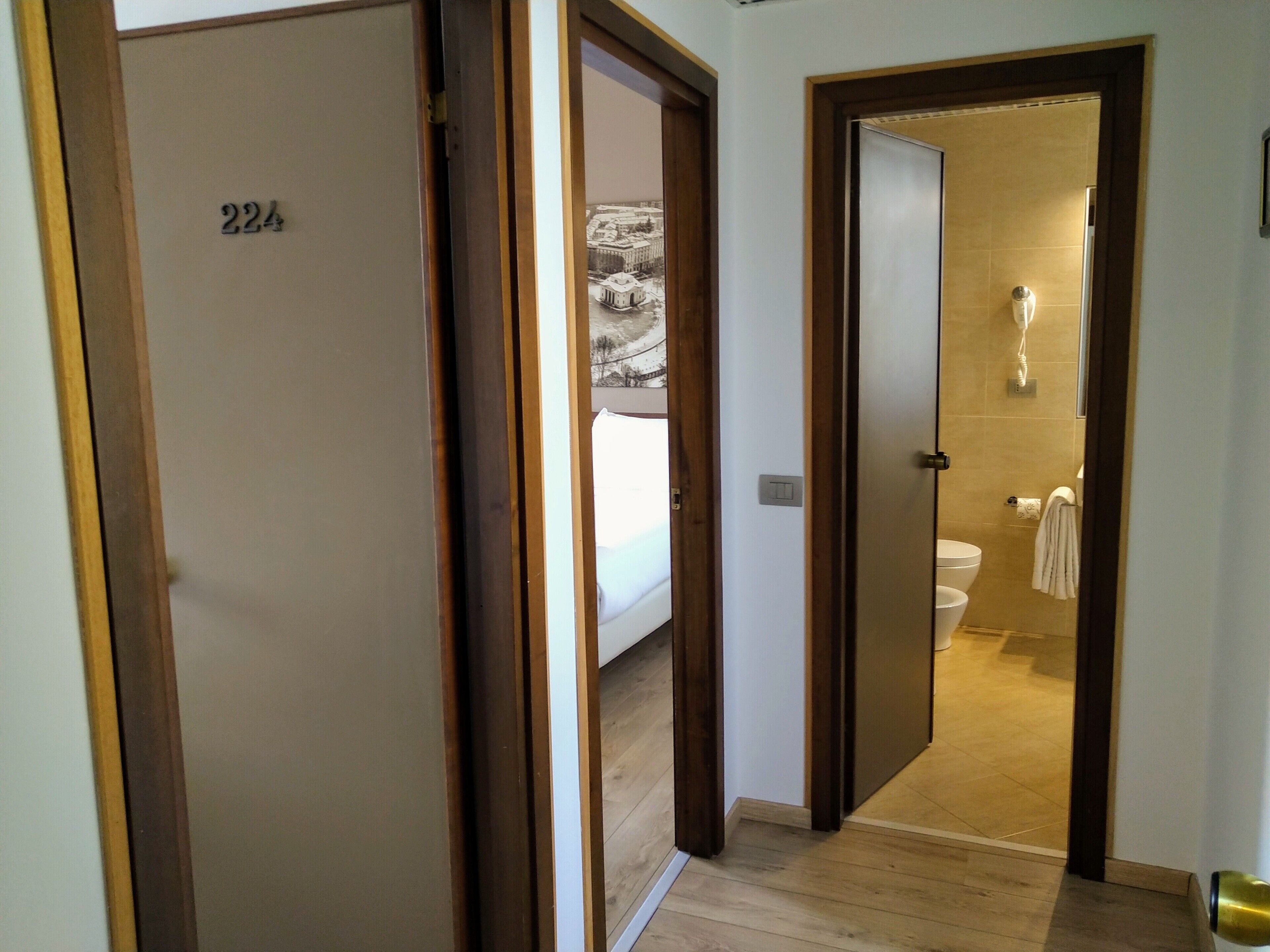 Ein Hotelzimmer mit einer Holztür mit der Aufschrift '224', ein Badezimmer mit Toilette und Handtuchhalter sowie ein Flur mit Holzboden.