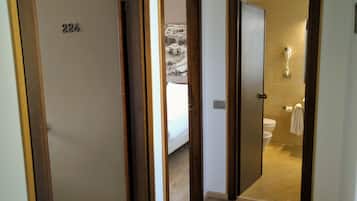 Ein Hotelzimmer mit einer Holztür mit der Aufschrift '224', ein Badezimmer mit Toilette und Handtuchhalter sowie ein Flur mit Holzboden.