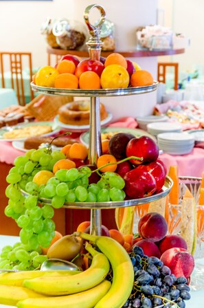 A multi-tiered fruit stand with various fruits and a bowl of pastries.