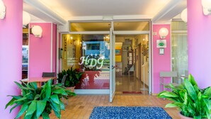 Entrada de hotel com porta de vidro, paredes cor de rosa e plantas dentro de casa.