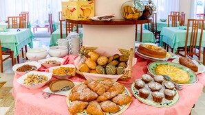 Mesa de buffet com diversos alimentos, pães e doces.