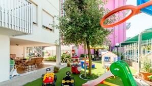 Uma área de recreação infantil com carrinhos de brinquedo, um escorrega e uma árvore.