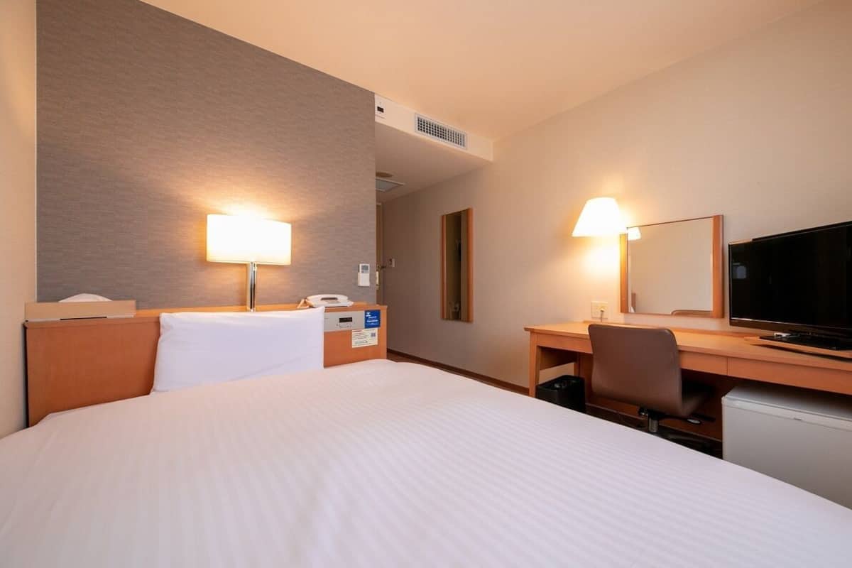 Habitación de hotel con cama, escritorio, televisión y dos lámparas de pared.
