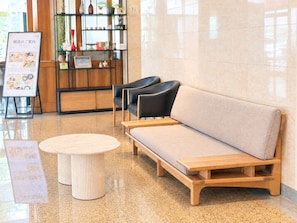 Un espace salon avec un canapé et des fauteuils, une petite table ronde et un panneau d’affichage présentant le menu.
