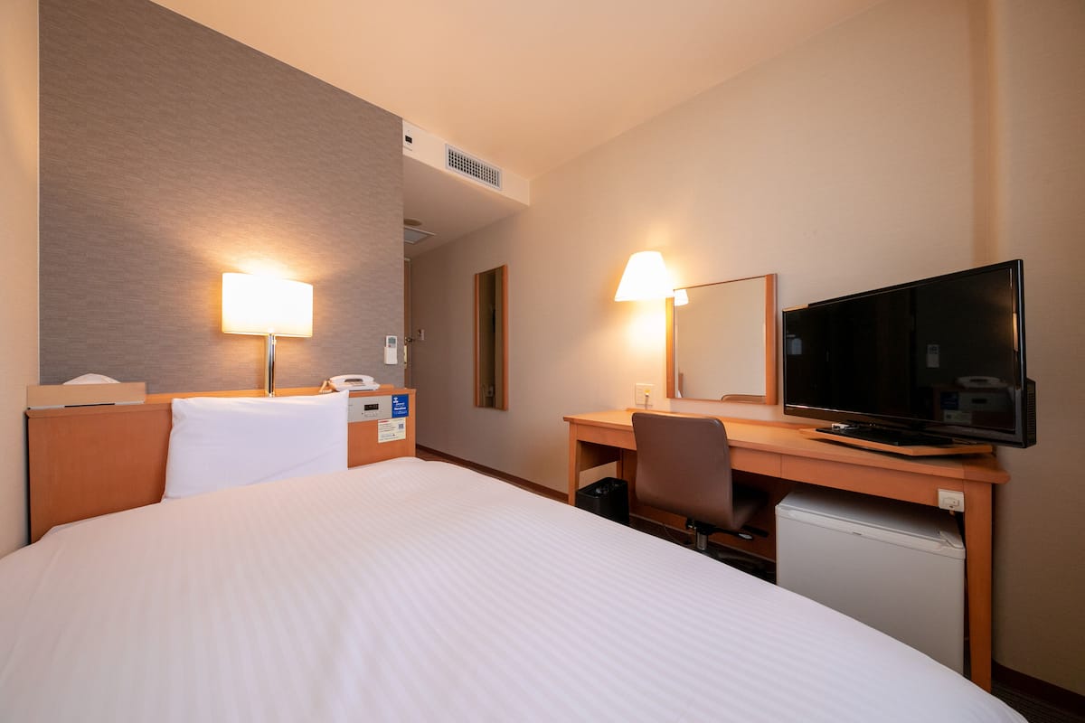 Habitación de hotel con cama, escritorio, silla, televisor y dos lámparas.