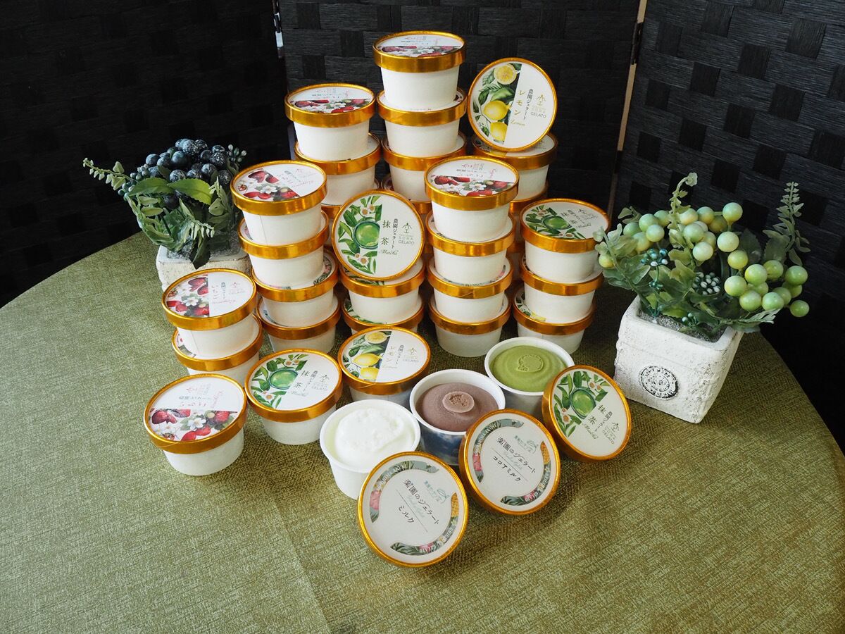 A table with multiple containers of food, each with a label. There are two potted plants on either side of the table.