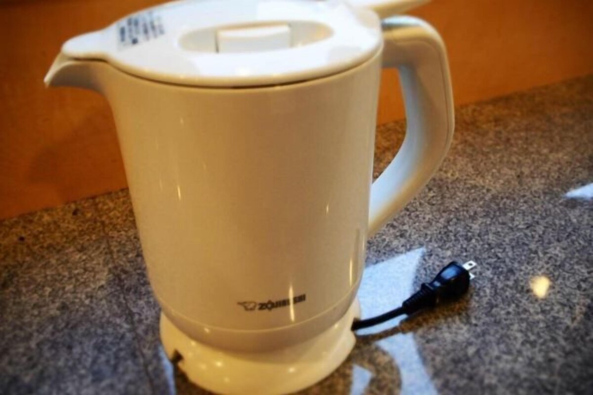 Une bouilloire électrique blanche, dotée d’une anse et d’un cordon d’alimentation, posée sur un plan de travail en granit.