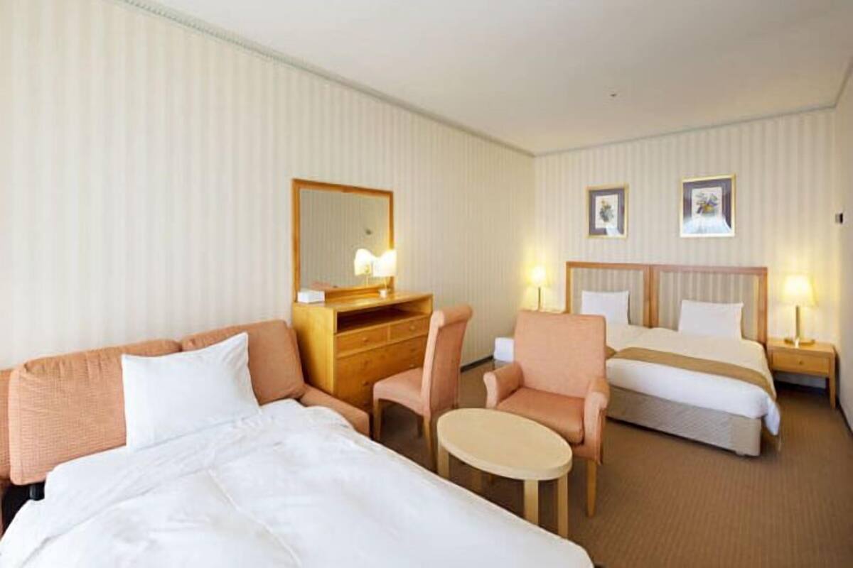 Une chambre d’hôtel avec deux lits, un canapé, une petite table et une commode.