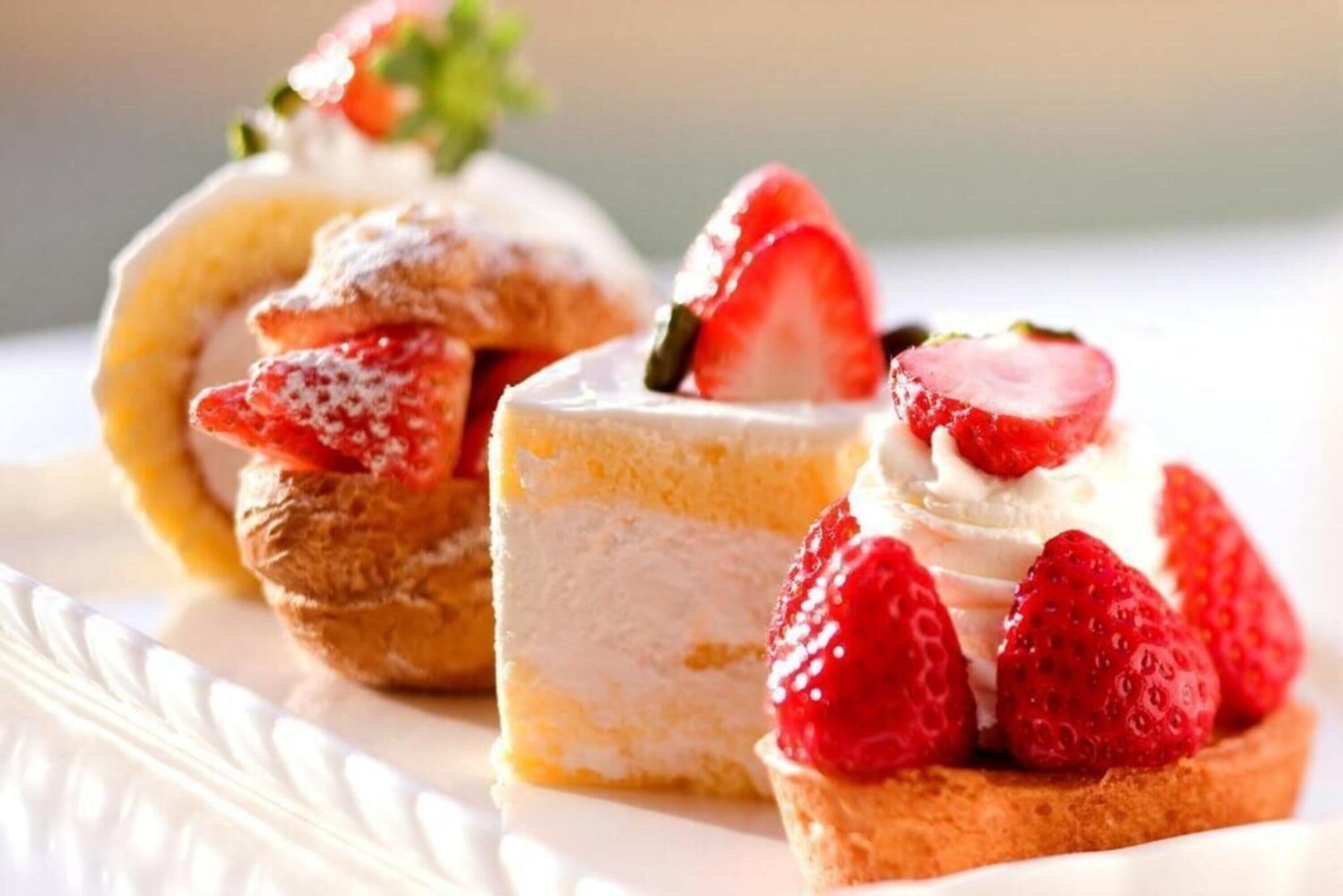 A dessert plate with three different types of pastries, including a cream puff, a slice of cheesecake, and a tart topped with strawberries.