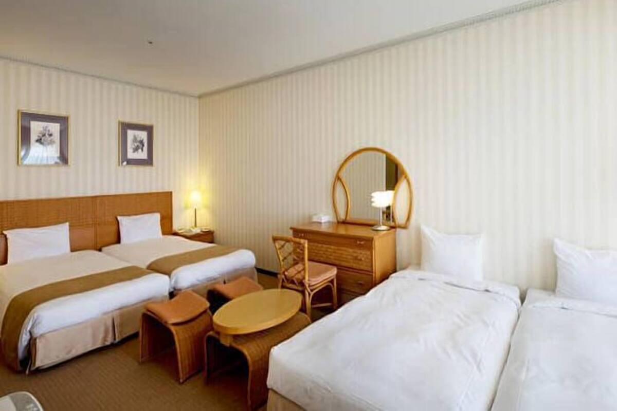 Une chambre d’hôtel avec deux lits, un bureau, une chaise, une table ronde et un miroir.