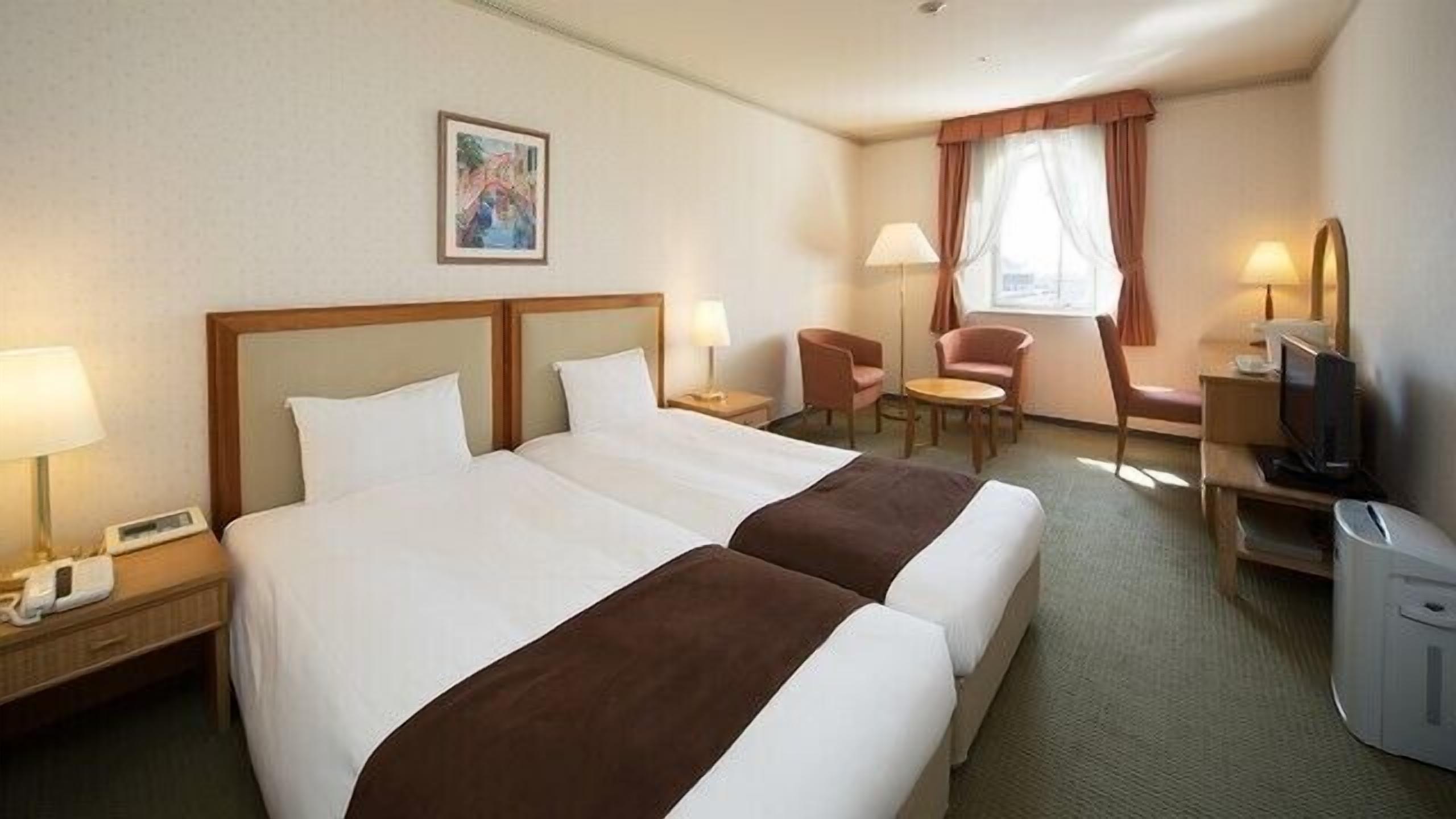 A hotel room with two beds, a desk with a computer, a chair, a lamp, and a painting on the wall.