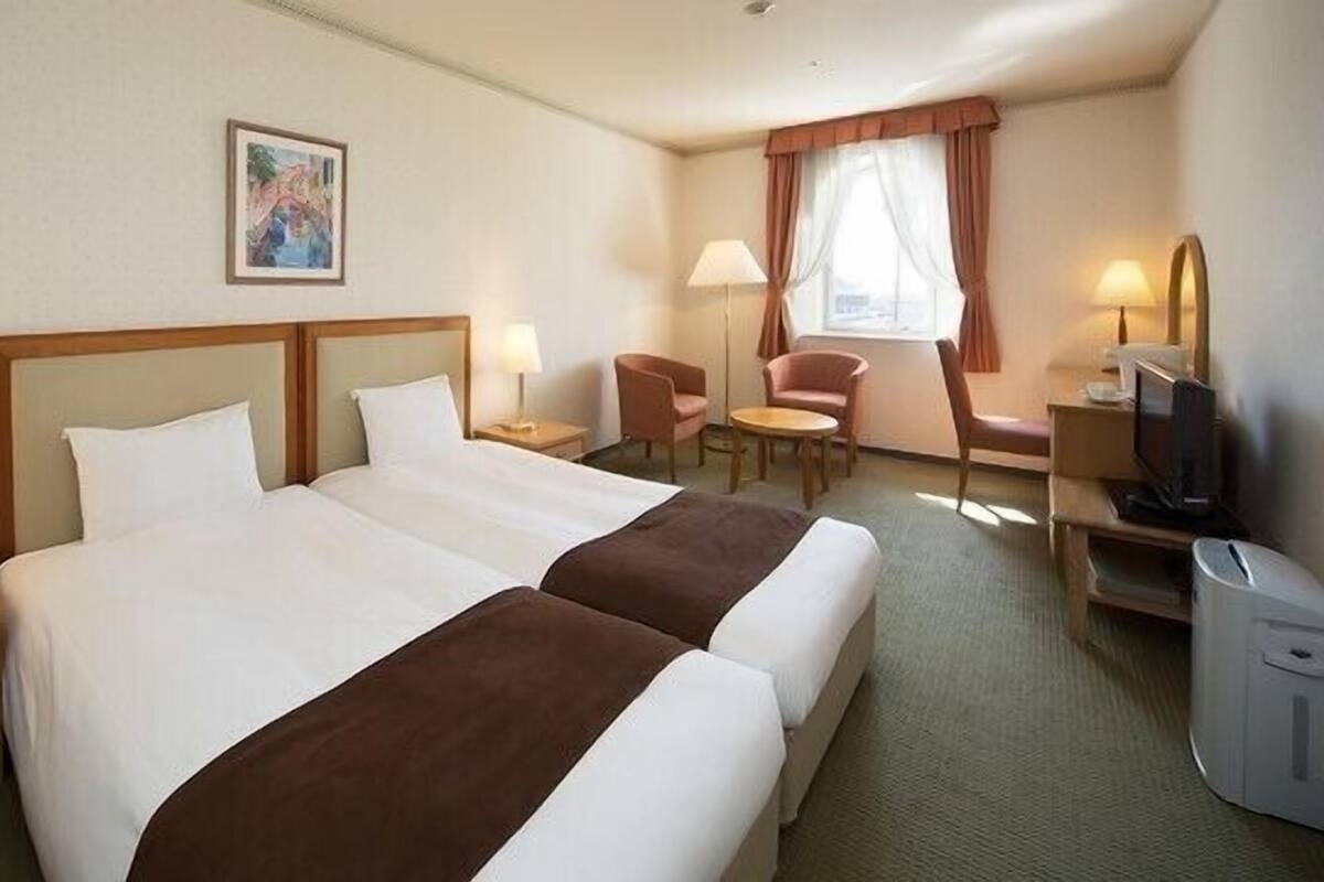 Une chambre d’hôtel avec deux lits, un bureau avec un ordinateur, une chaise, une lampe et un tableau au mur.