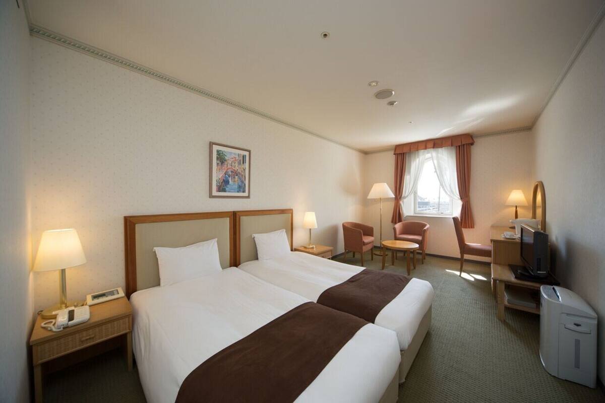 Une chambre d’hôtel avec deux lits, un bureau avec un ordinateur, une chaise, une télévision et un téléphone sur la table de chevet.