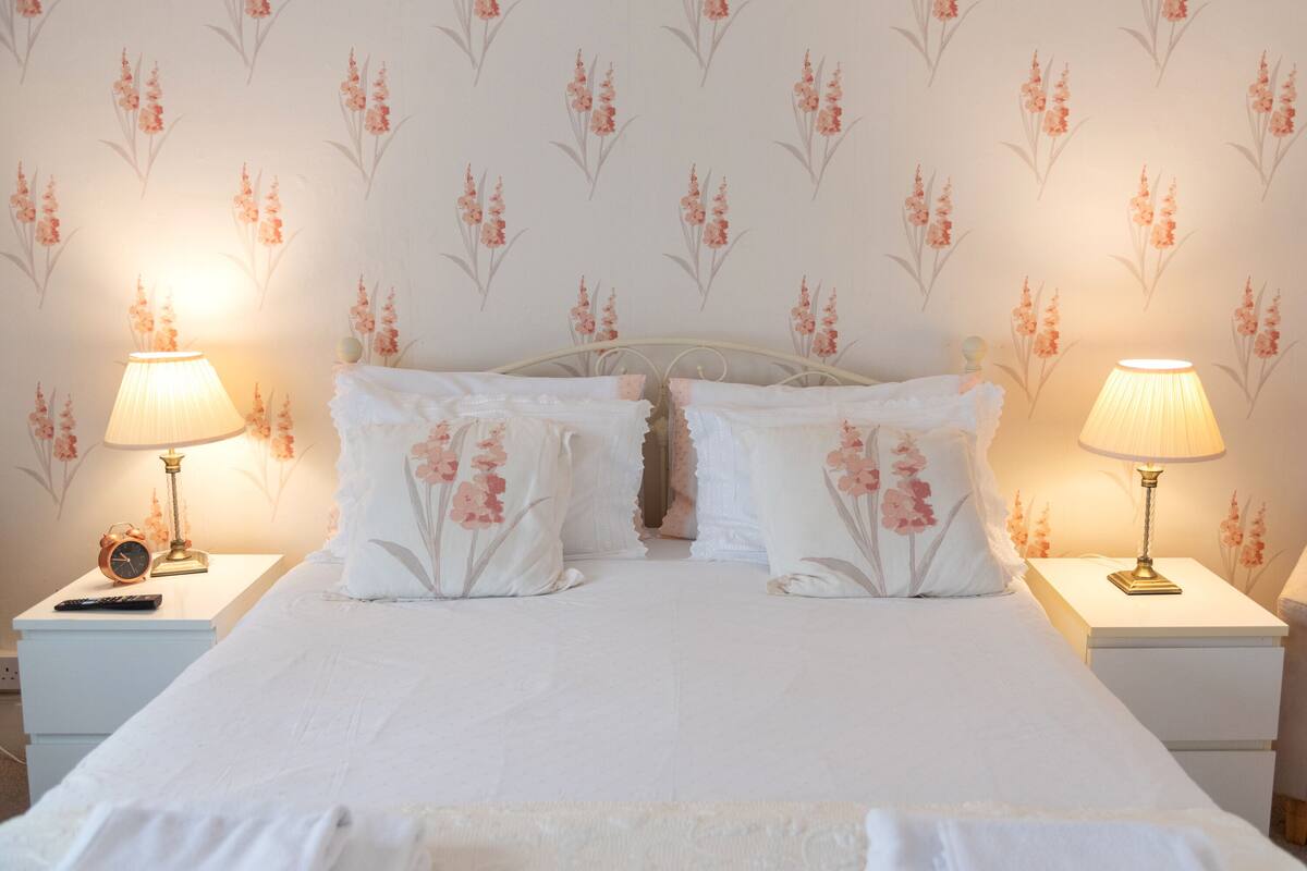 A neatly made bed with floral pillows and two bedside lamps on white nightstands.