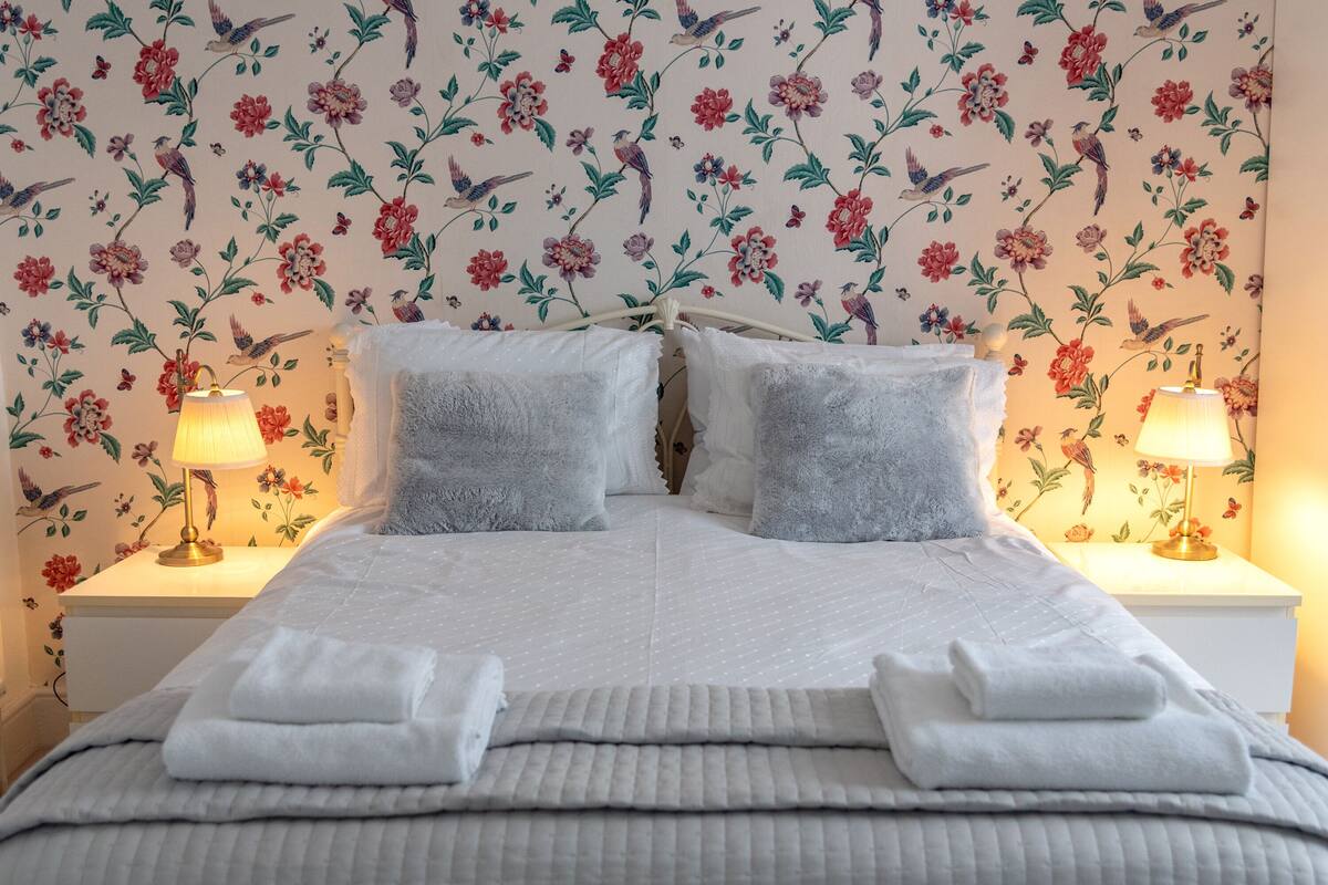A neatly made bed with white linens and pillows, flanked by two bedside tables with lamps.