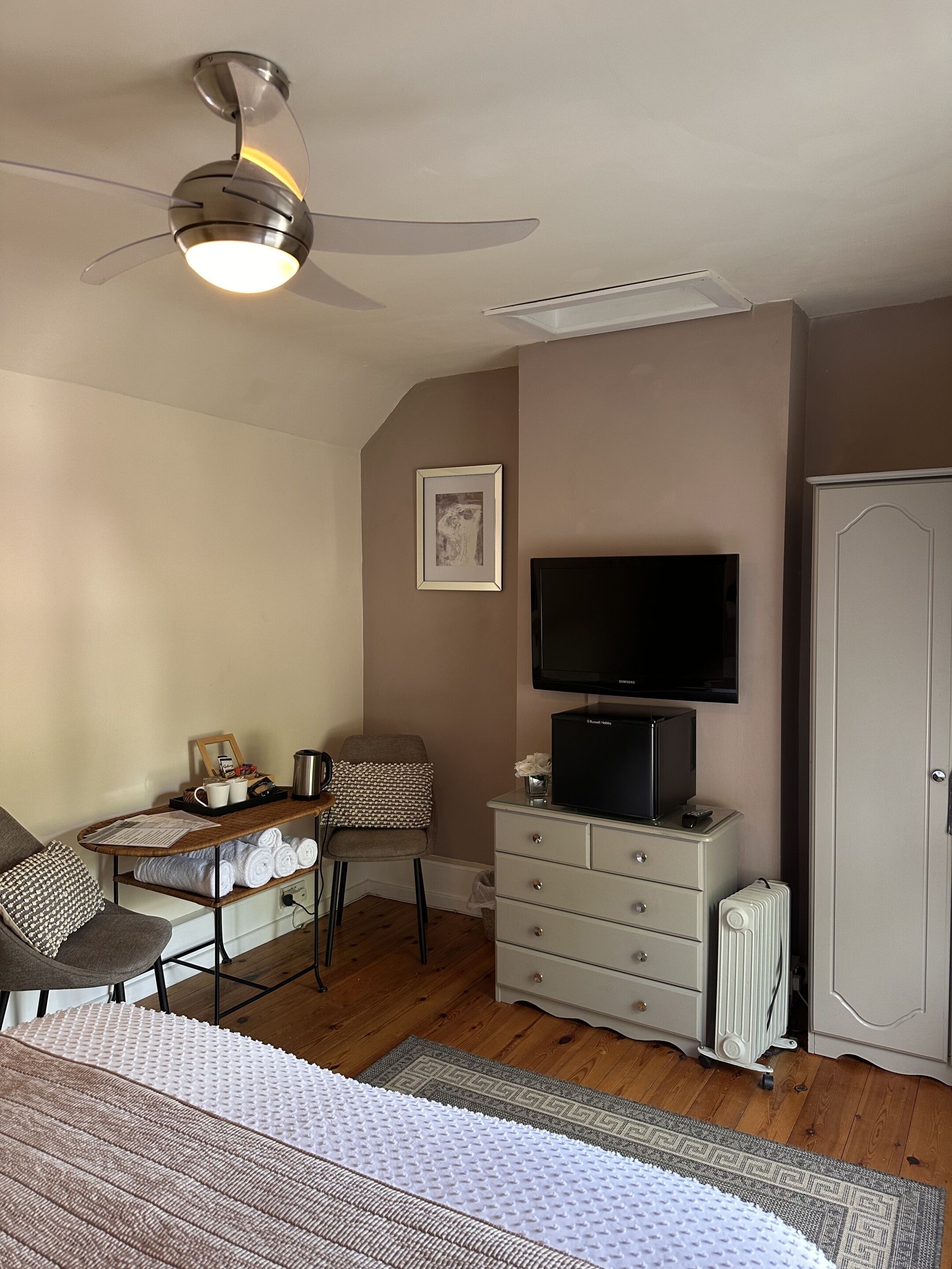 A bedroom with a bed, a desk with a chair, a television, a wardrobe, and a ceiling fan.