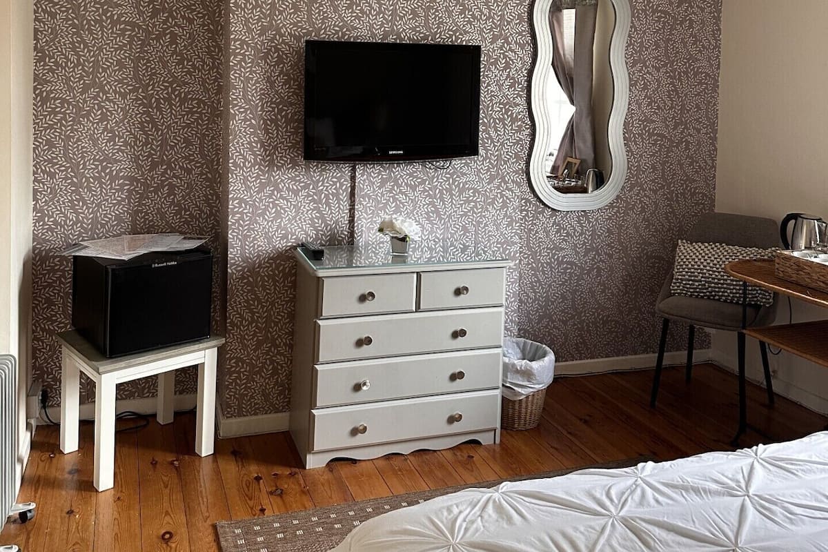 Quarto com cama, cômoda, televisão e ventoinha no teto, além de papel de parede estampado.