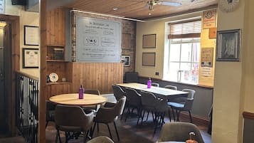 A restaurant interior with wooden tables and chairs, a whiteboard with text, and a window with blinds.