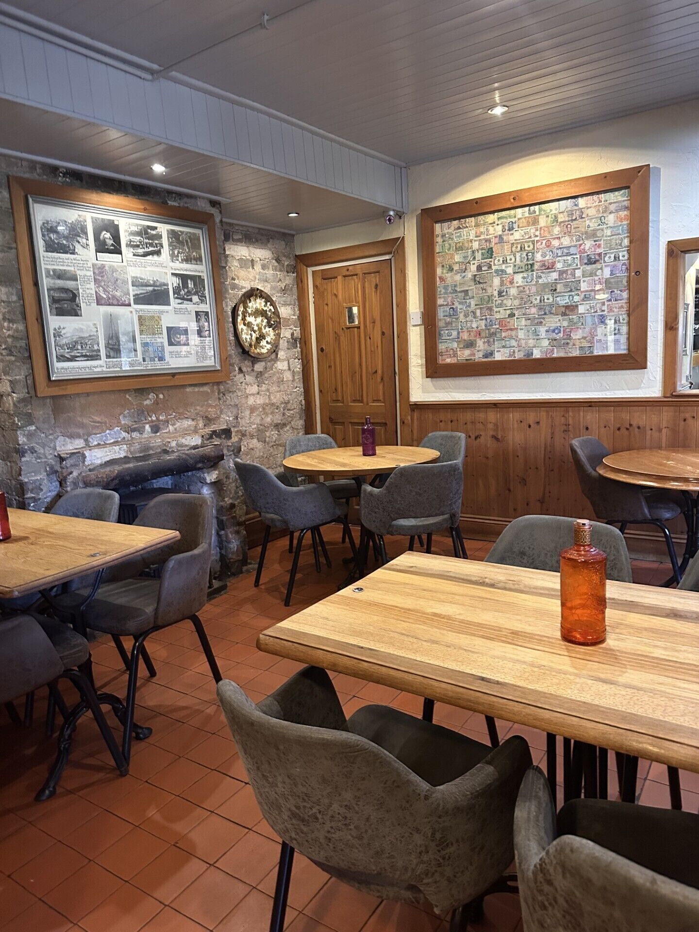 Un restaurante acogedor con decoración rústica, que cuenta con mesas y sillas de madera, una pared de piedra y un tablón de anuncios con fotografías.