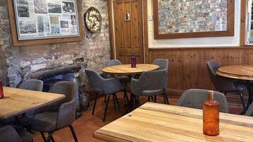 Un restaurante acogedor con decoración rústica, que cuenta con mesas y sillas de madera, una pared de piedra y un tablón de anuncios con fotografías.