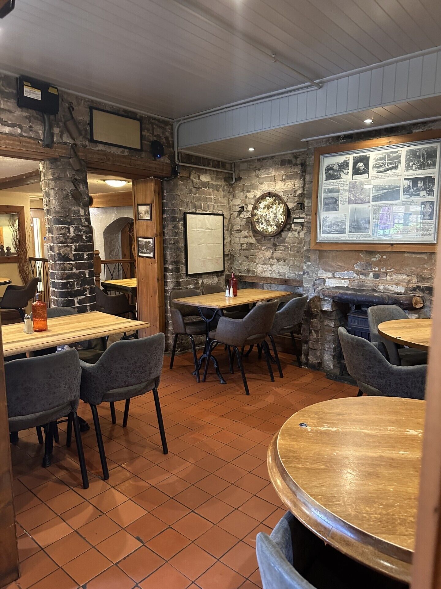 A restaurant with rustic stone walls, wooden tables, and grey upholstered chairs.