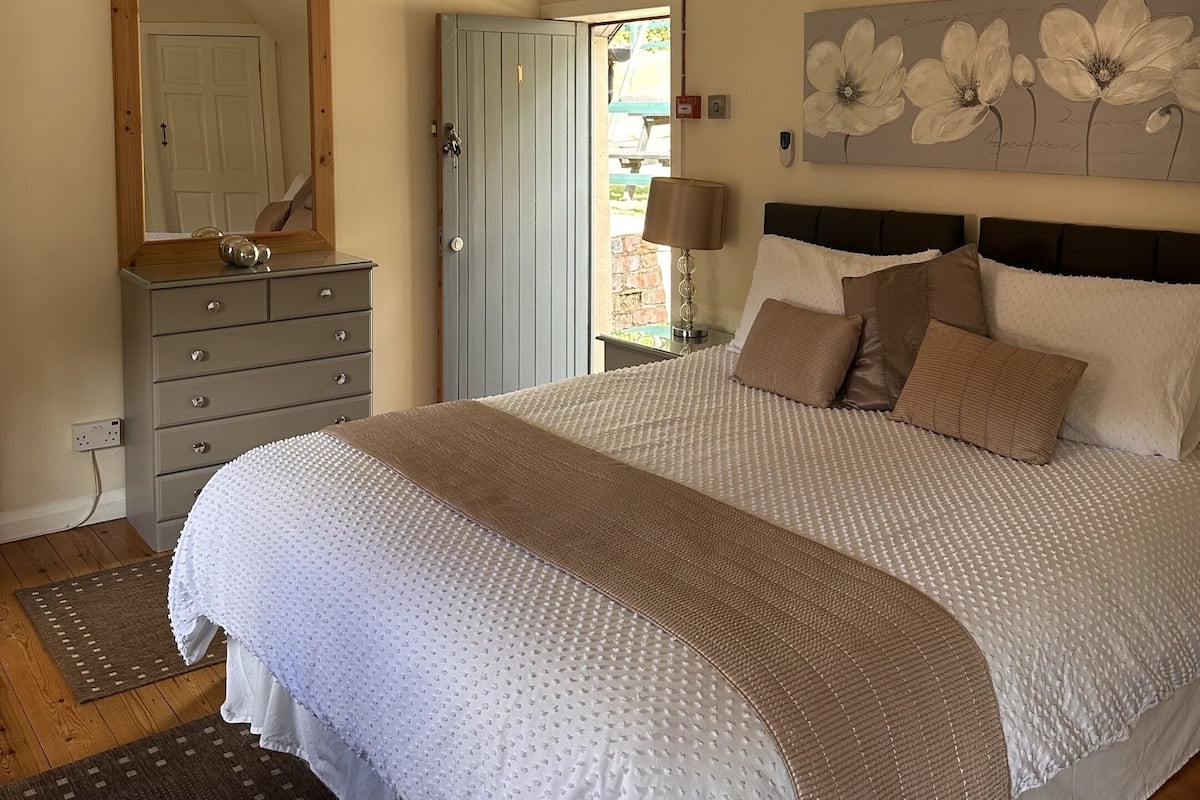 Quarto com cama, penteadeira, ventilador de teto e porta que dá para o exterior.