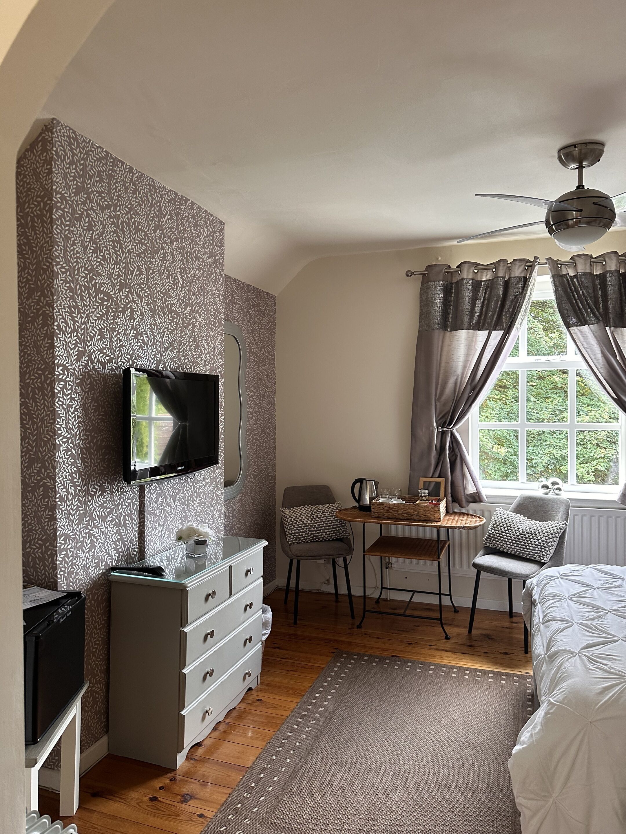 A bedroom with a TV, a desk, a chair, a bed, and a window with curtains.