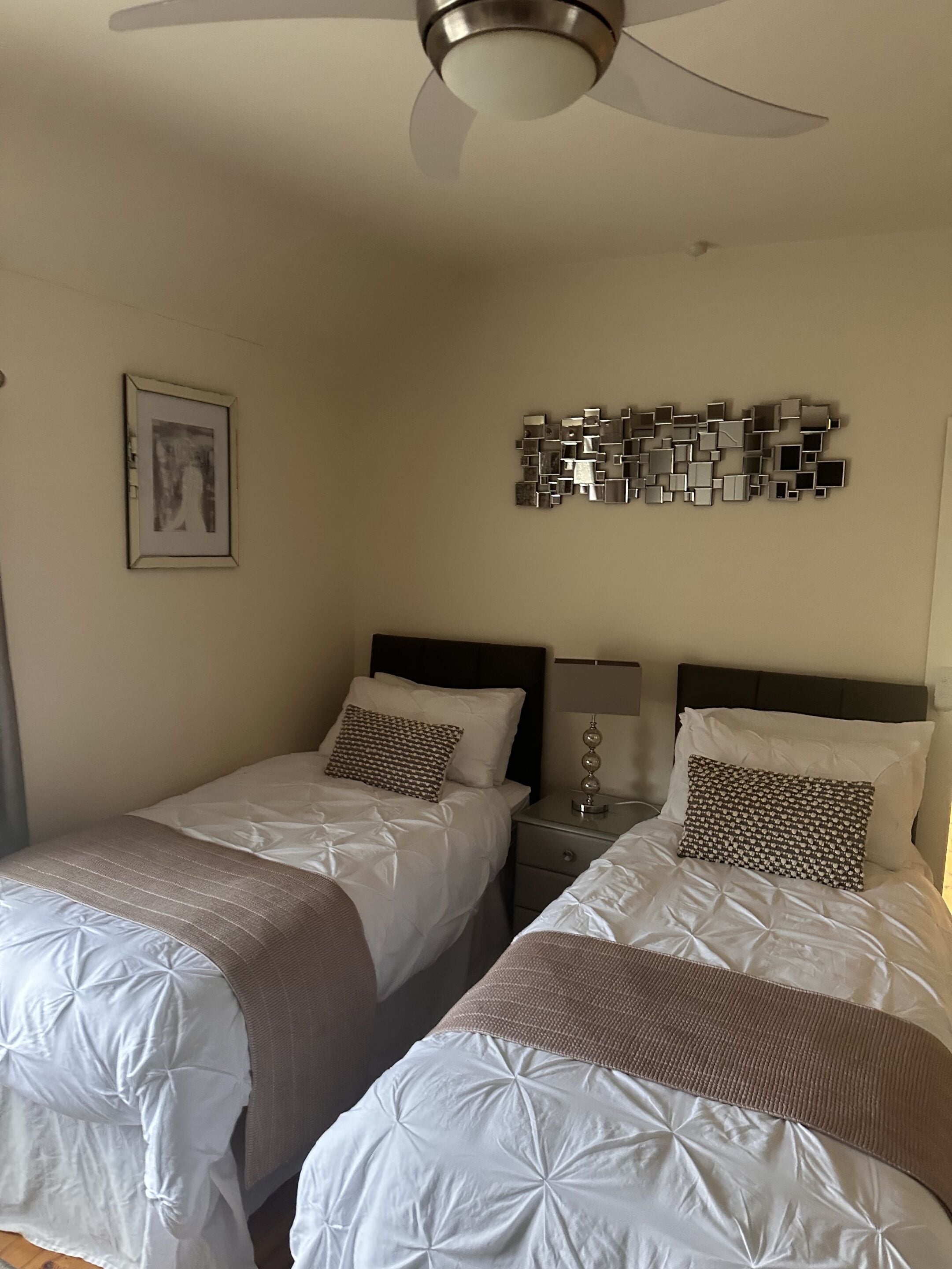 A hotel room with two beds, a ceiling fan, a wall-mounted artwork, and a decorative metal piece.