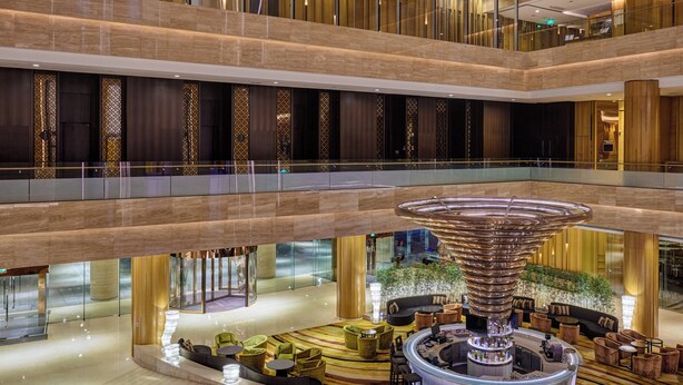 A multi-level hotel lobby with a central circular bar area, seating arrangements, and a decorative water feature.
