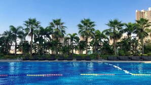 A swimming pool with clear blue water, surrounded by palm trees and lounge chairs.