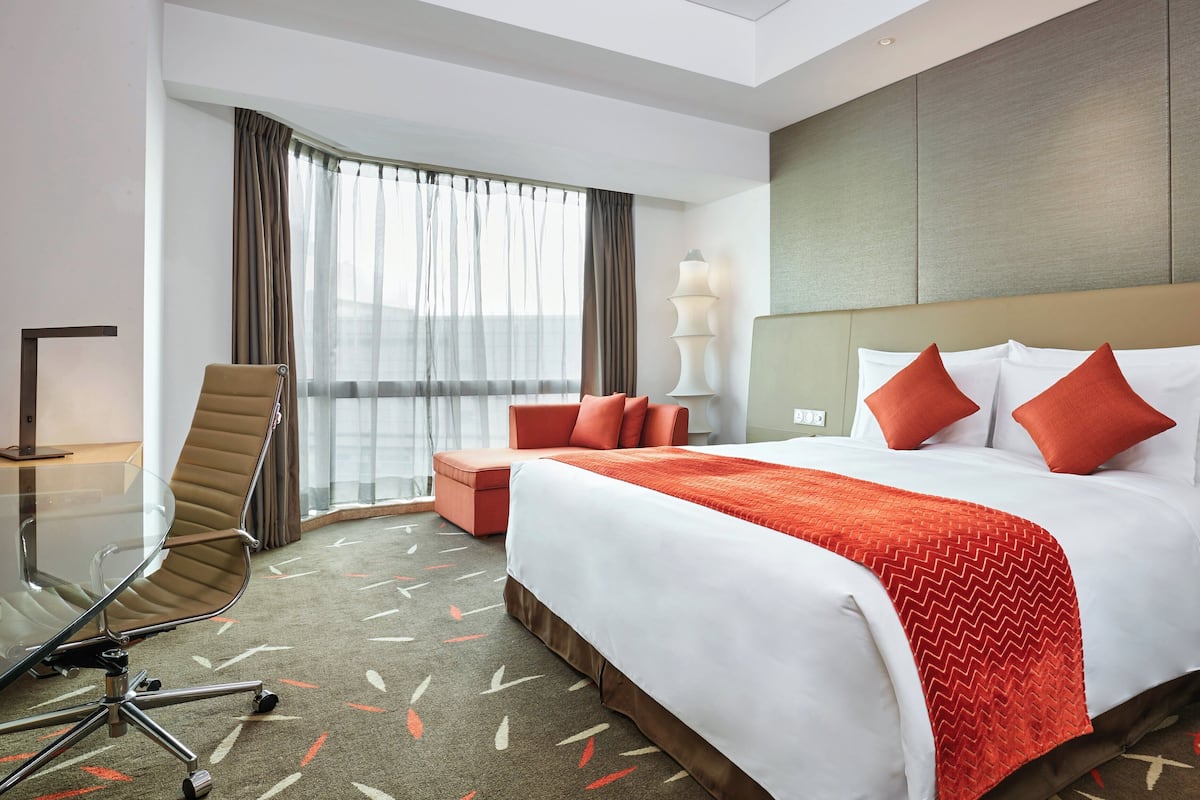 Une chambre d’hôtel avec un grand lit, un coin salon, une table en verre et une vue sur la ville.