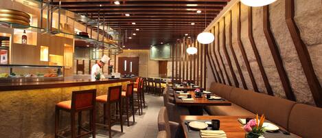 A restaurant interior with a bar area, seating, and a chef preparing food.