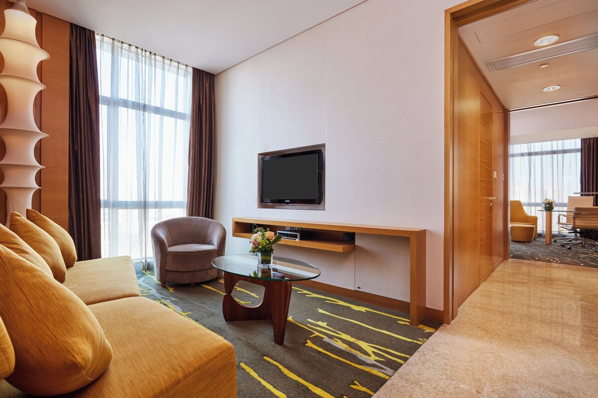 A hotel room with a sofa, armchair, and a glass coffee table.