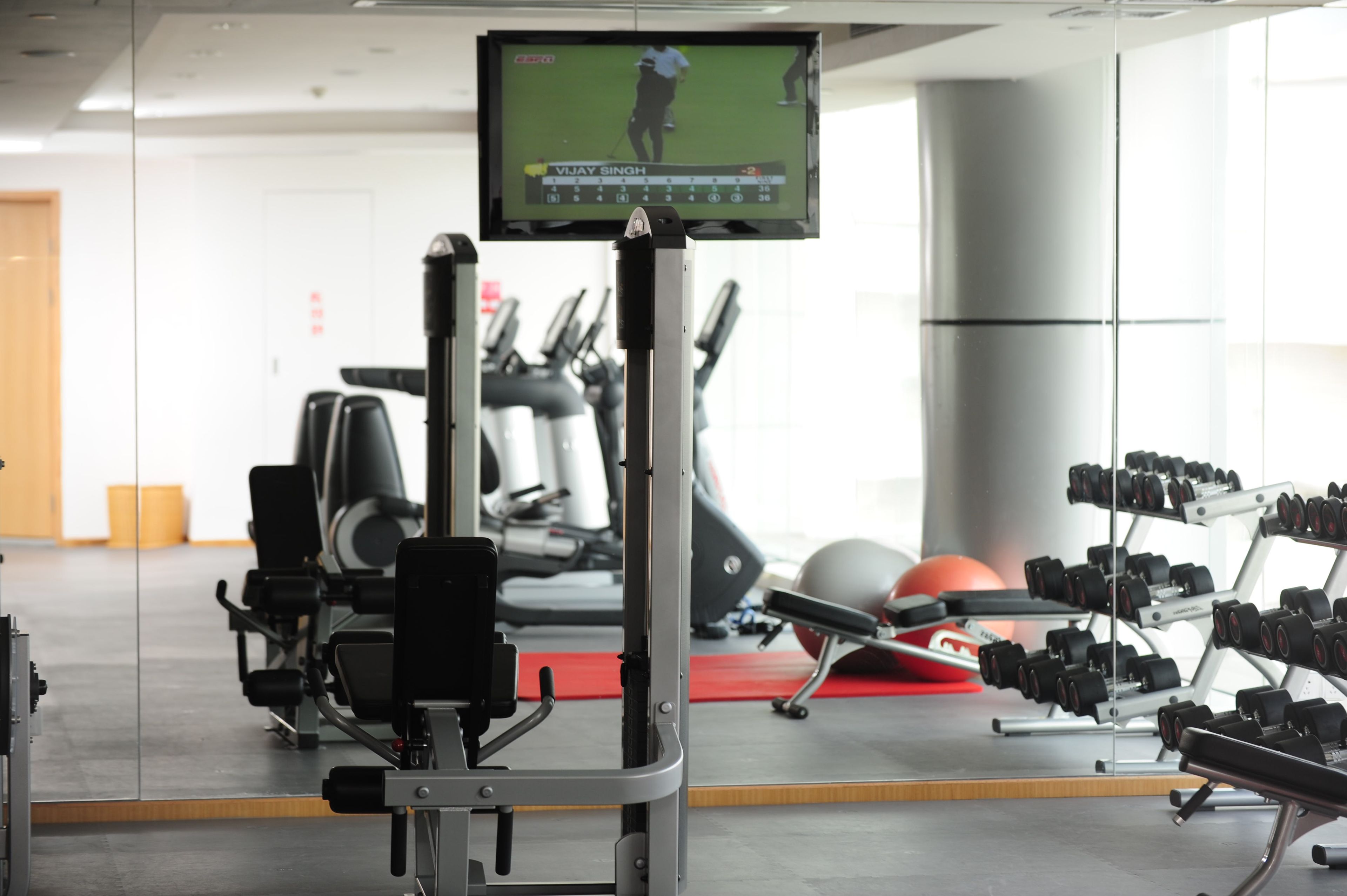 A gym with exercise equipment, a television displaying a golf game, and a red exercise ball.