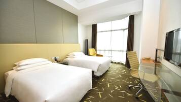 A hotel room with two beds, a desk with a flat-screen TV, a chair, and a large window with curtains.