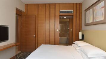 A hotel room with a bed, a TV, a wooden wardrobe, and a shower area.
