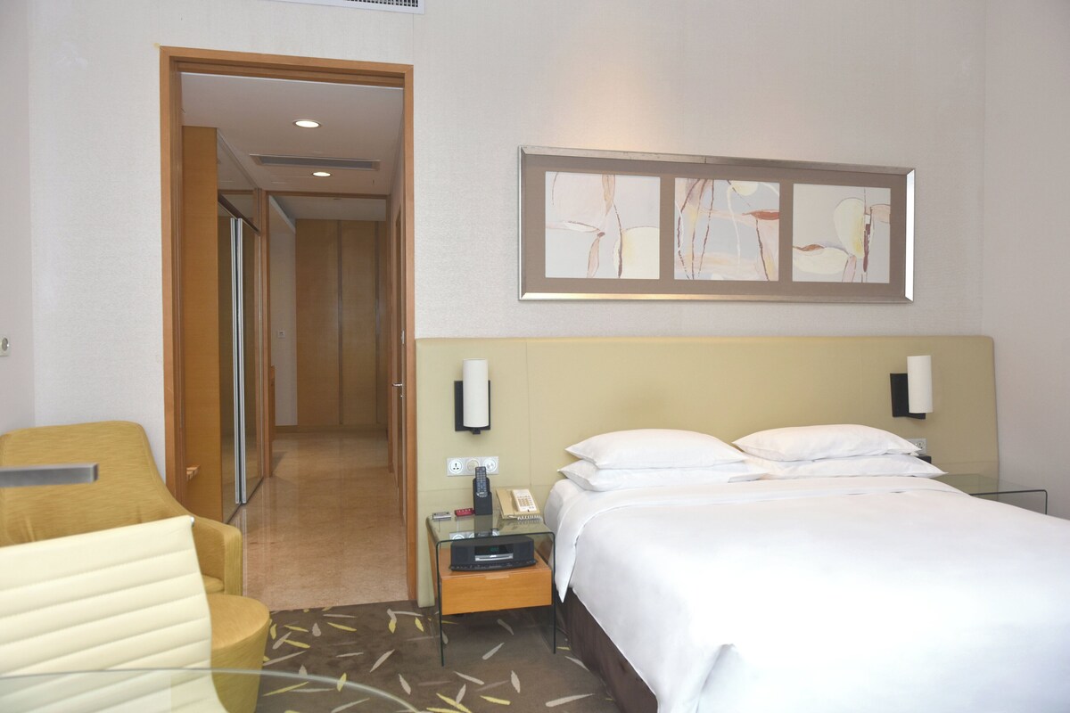 A hotel room with a bed, bedside table, lamp, and a painting on the wall.