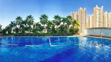 Una piscina con agua azul cristalina, rodeada de palmeras y altos edificios residenciales.