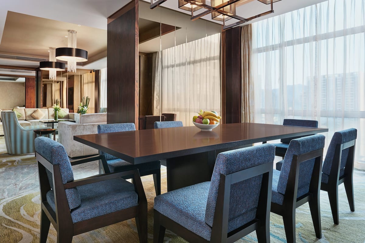 Un espace de restauration moderne dans un hôtel, avec une longue table en bois, des chaises à l’assise rembourrée de couleur bleue et un saladier de fruits posé sur la table.