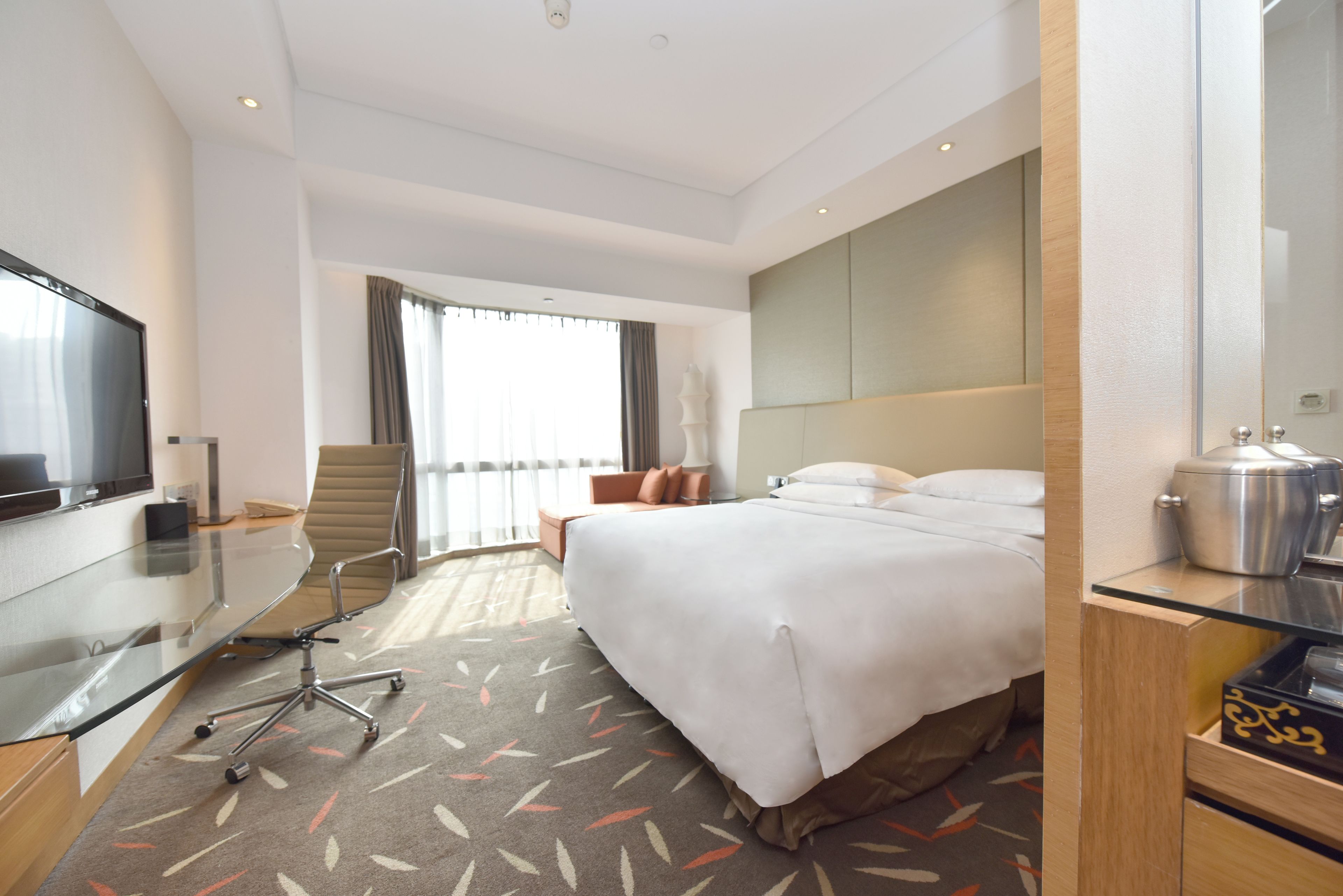 Une chambre d’hôtel avec un lit, un bureau équipé d’un ordinateur, une télévision et une fenêtre avec des rideaux.