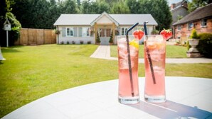 Two tall glasses of pink beverage with ice and fruit garnishes on a white table in a backyard with a house in the background. - Slaters Country Inn (Newcastle-Under-Lyme)