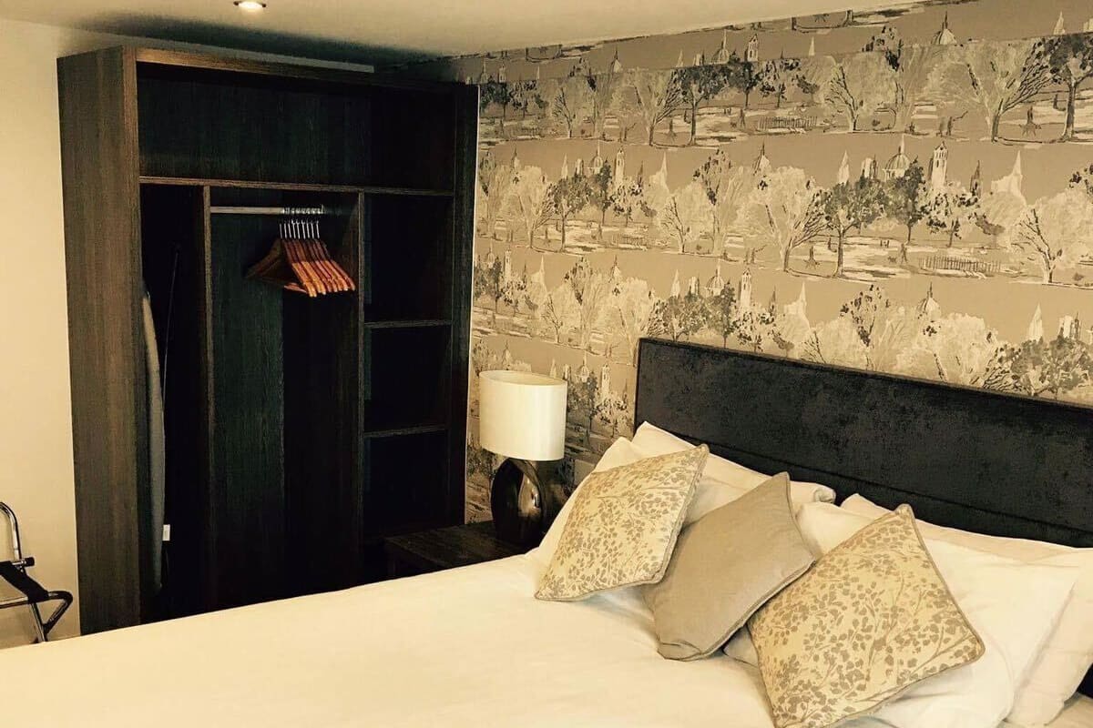 A hotel room with a large bed, a wardrobe, and a nightstand with a lamp.