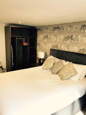 A hotel room with a large bed, a wardrobe, and a nightstand with a lamp.