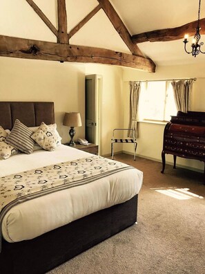 A bedroom with a large bed, a wooden ceiling, a nightstand, a lamp, a chair, and a dresser.