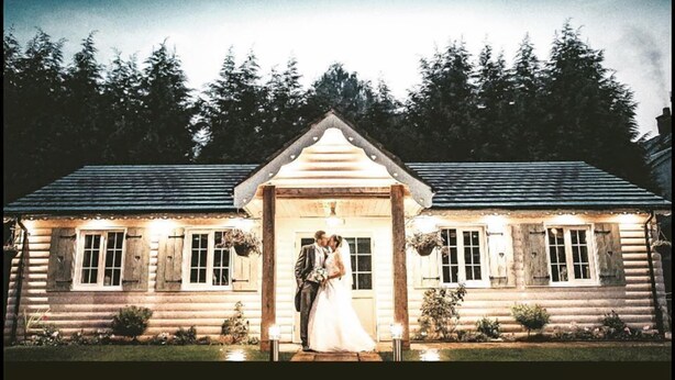 A log cabin wedding venue with a central archway, surrounded by a forest. - Slaters Country Inn (Newcastle-Under-Lyme)