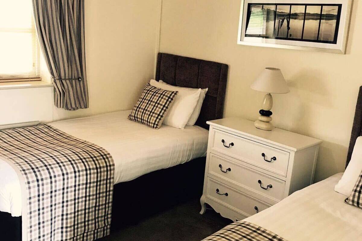 A bedroom with two beds, a nightstand, a lamp, and a framed picture on the wall.